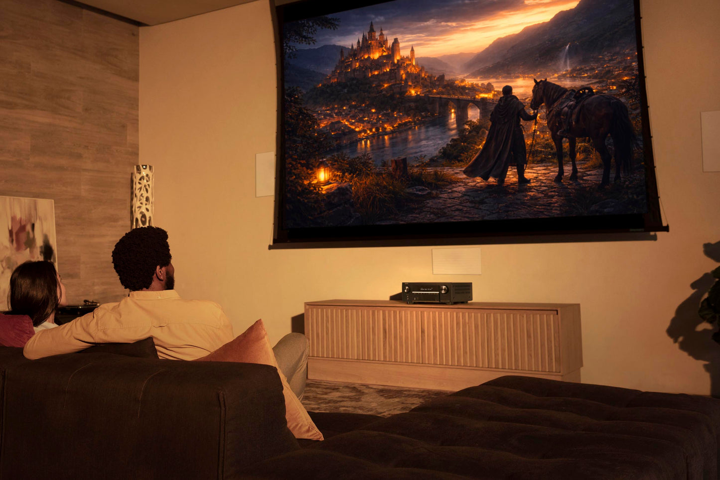 Two people sitting on a couch watching a movie or TV show projected onto a wall.
