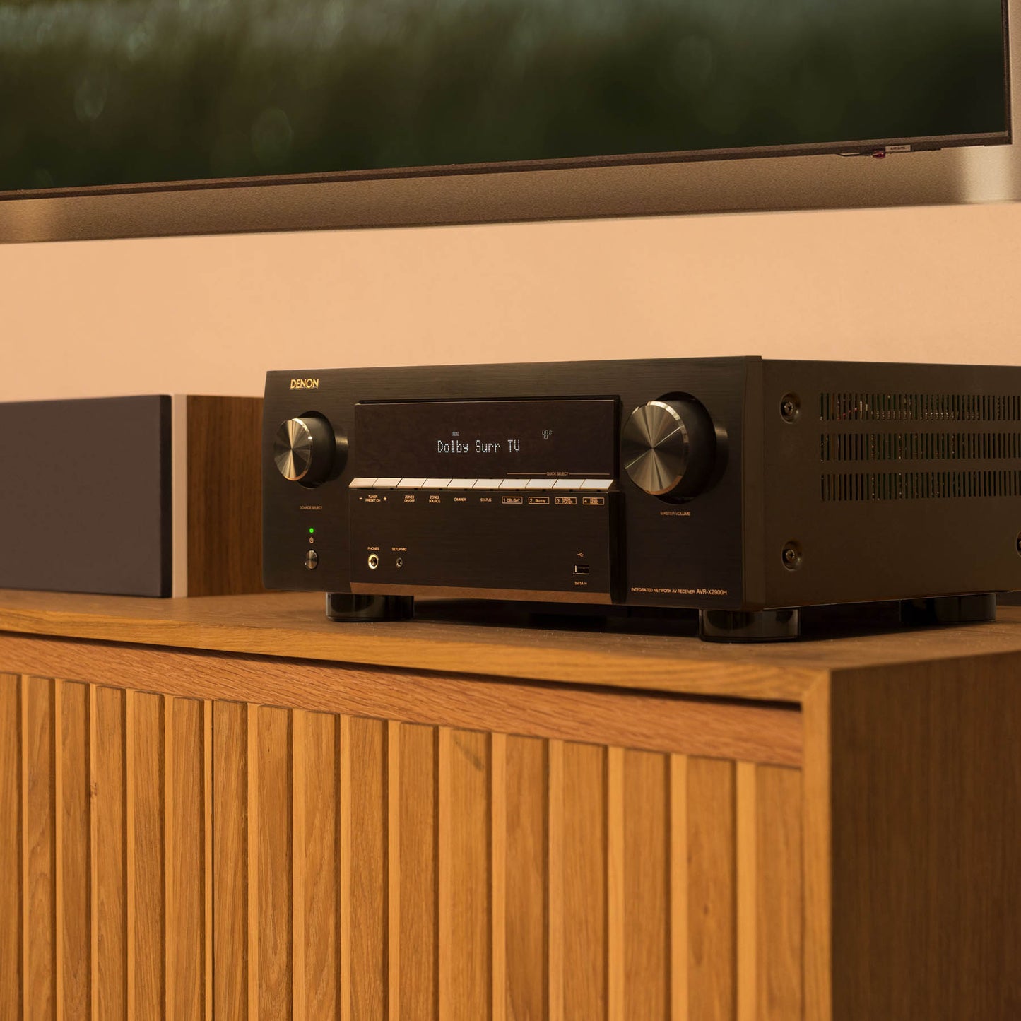 Denon amplifier on a wooden cabinet with a television in the background
