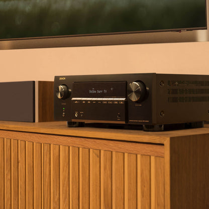 Denon amplifier on a wooden cabinet with a television in the background