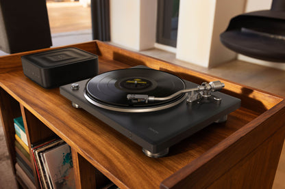 Turntable on a wooden shelf with records in a cozy room.