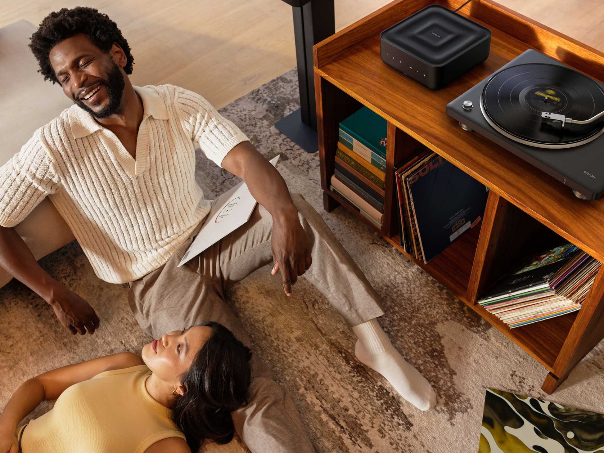 Man and woman sitting on a rug in a living room with a record player and records.