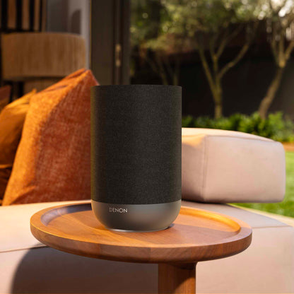 Black Denon speaker on a wooden tray with outdoor furniture in the background