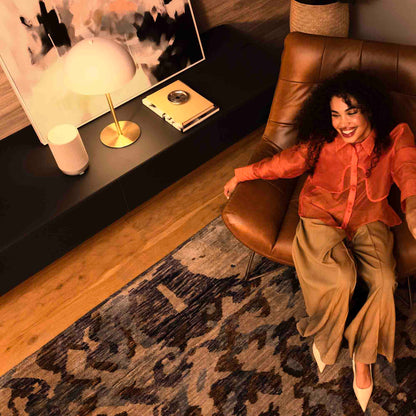 Woman sitting on a brown leather chair in a cozy living room listening to Denon Home 200 Speaker in white finish