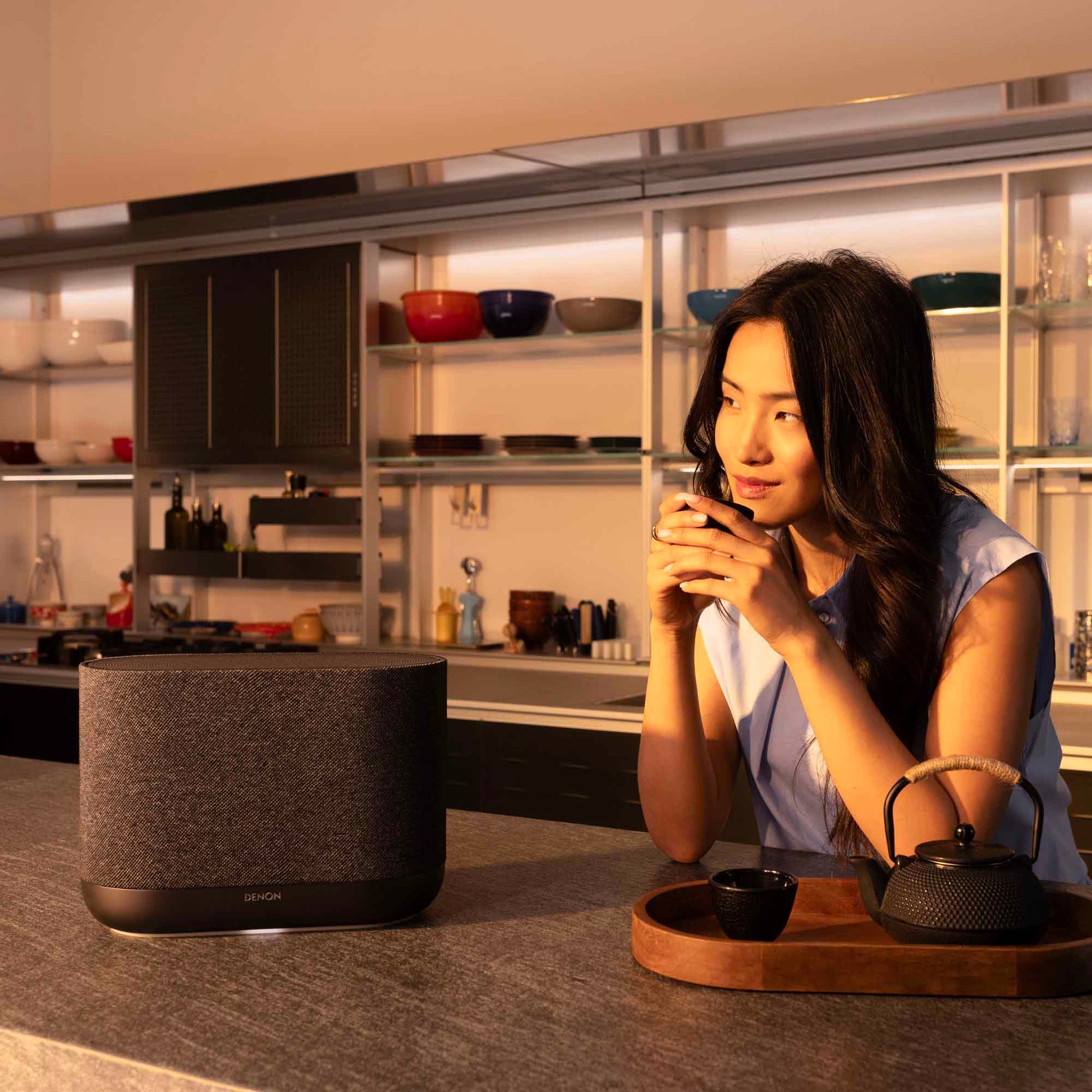 Lady leaning on kitchen bench next to black black Denon Home 400 wireless smart speaker