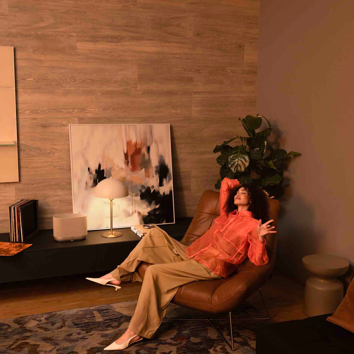Woman sitting on a brown leather chair in a cozy living room with abstract art and decor.