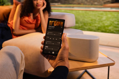 Person using a smartphone app to control a smart speaker outdoors