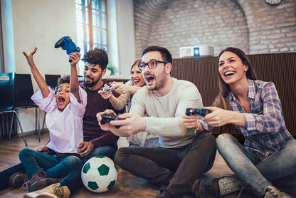 A group of friends sitting on the floor in a living room, playing video games. Projecter in background.