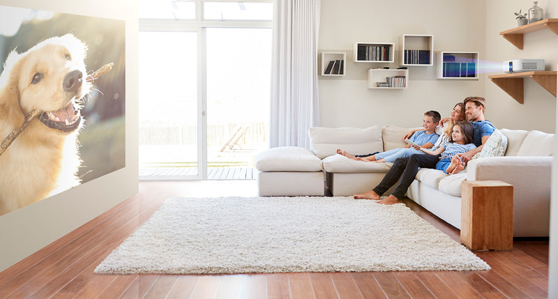 Family sitting on a couch in a modern living room with a dog on a screen
