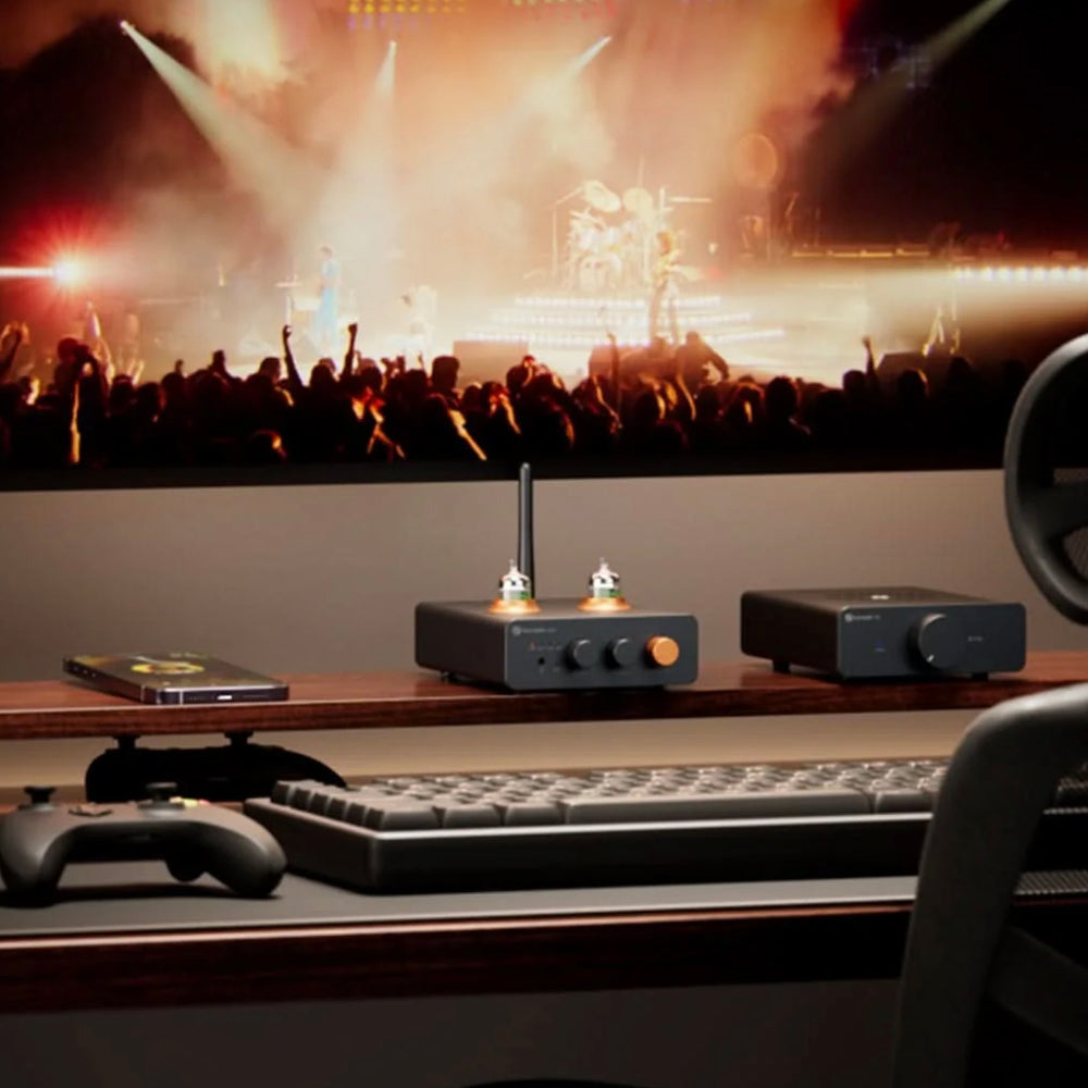 Desk setup with audio equipment and phone, facing a concert scene on a large screen.