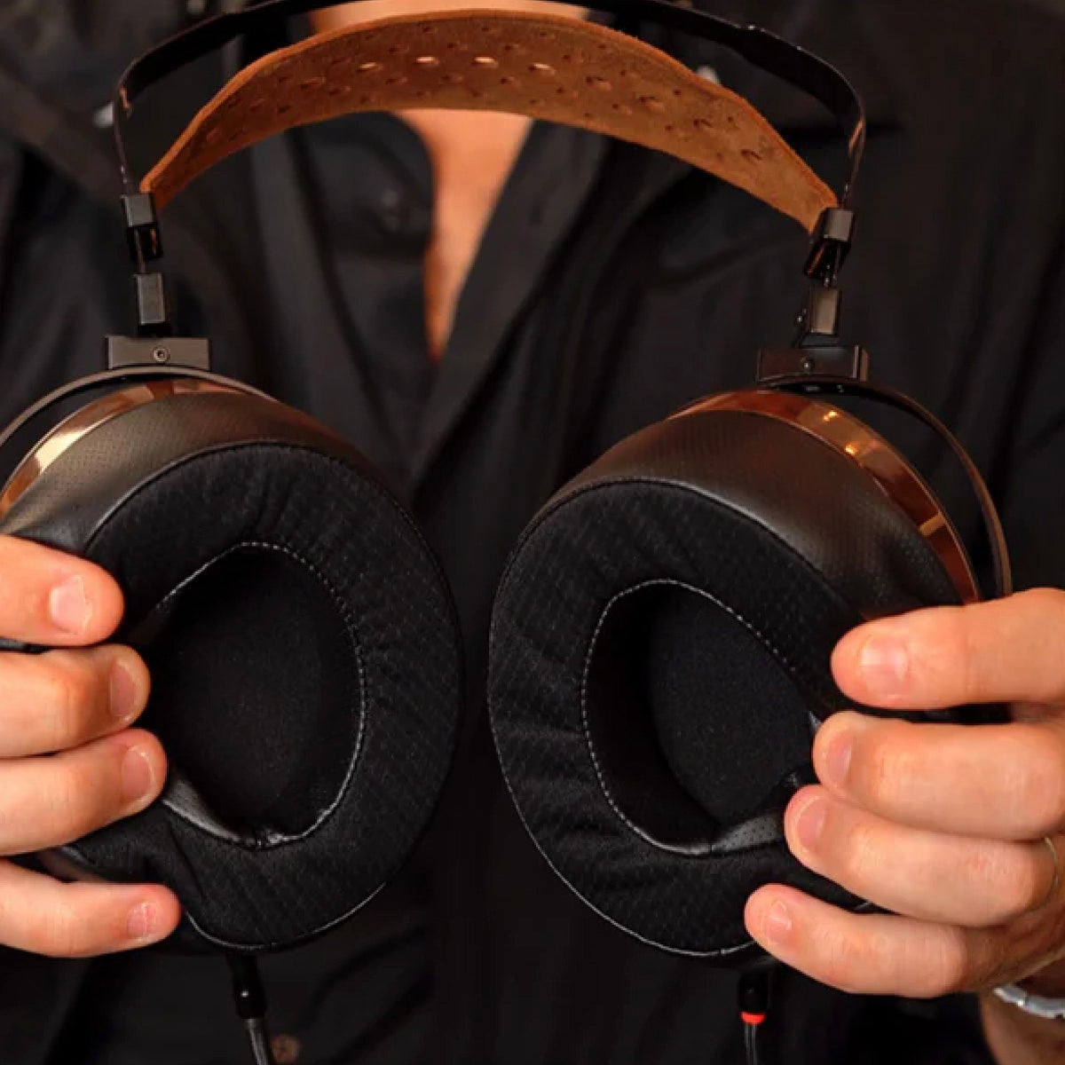 Person holding a pair of black headphones with brown leather straps against a dark background