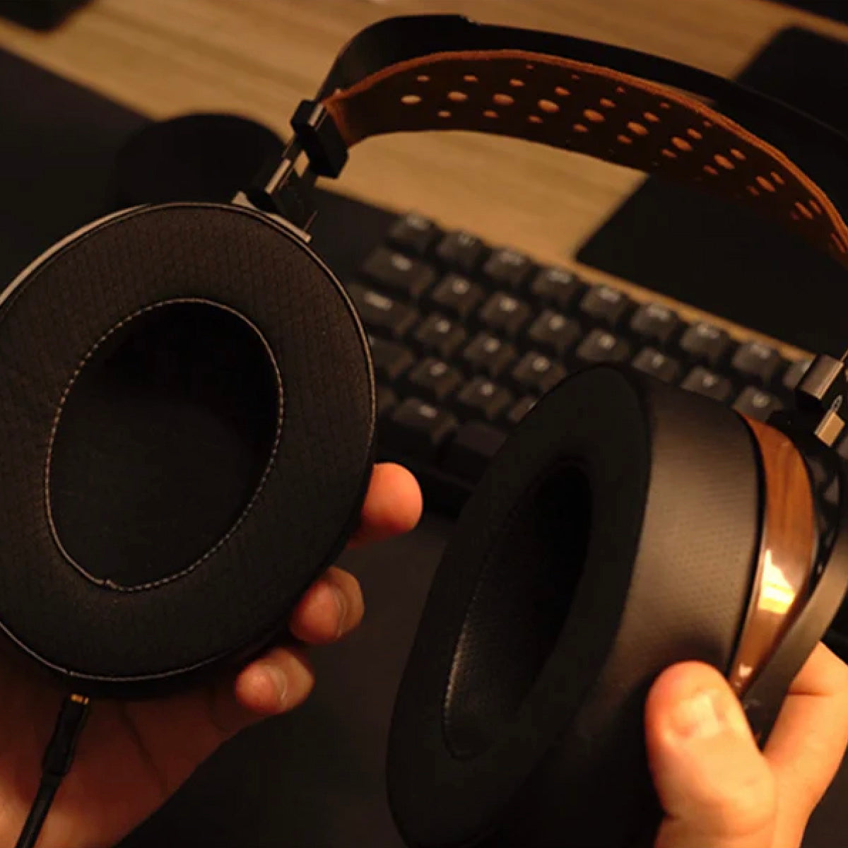 Close-up of a person holding a pair of black headphones with a keyboard in the background.