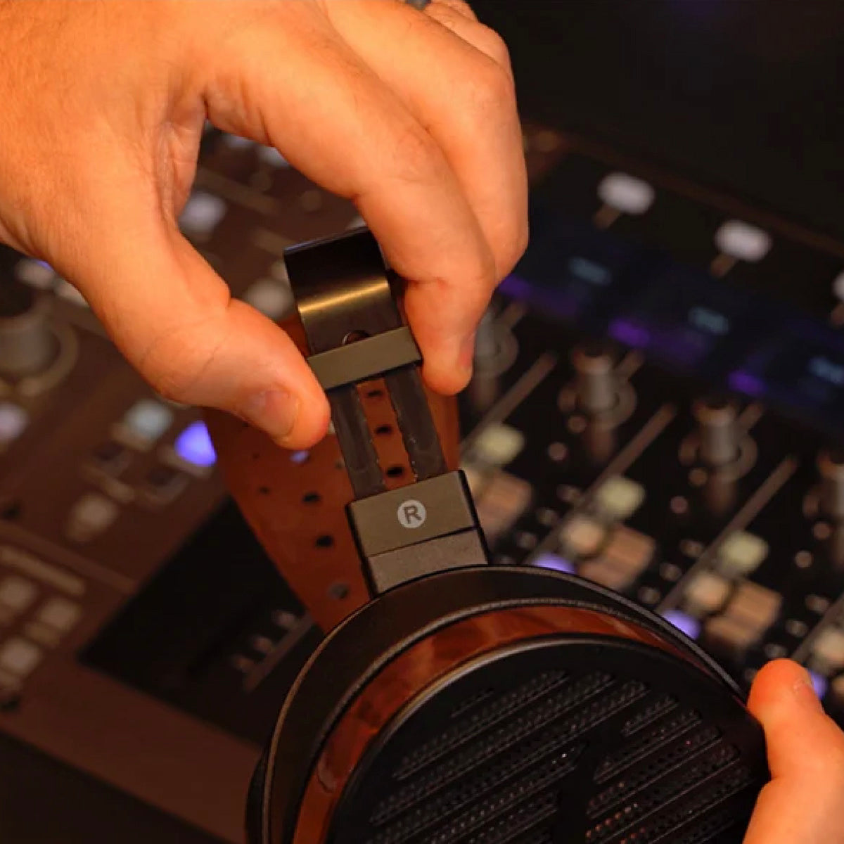 Person holding a pair of headphones with a blurred background of audio equipment