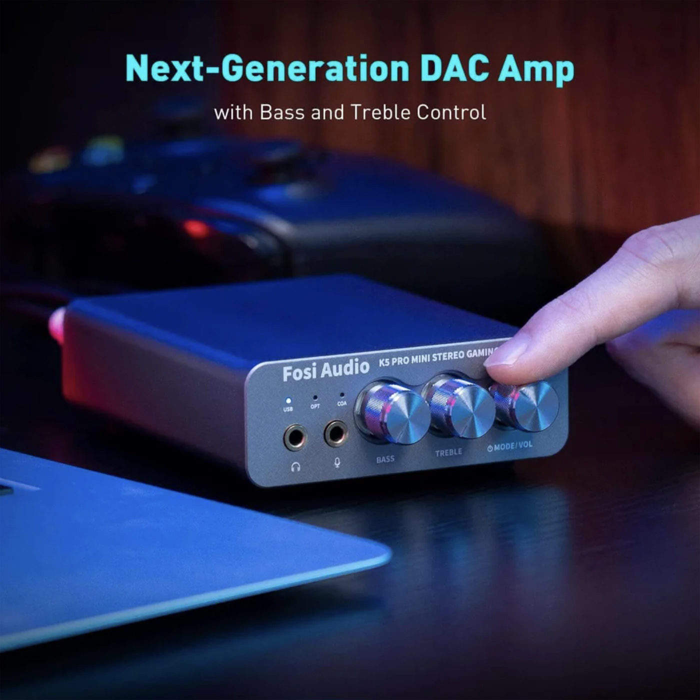 Fosi Audio DAC Amp with knobs on a dark surface, blurred gaming setup in the background
