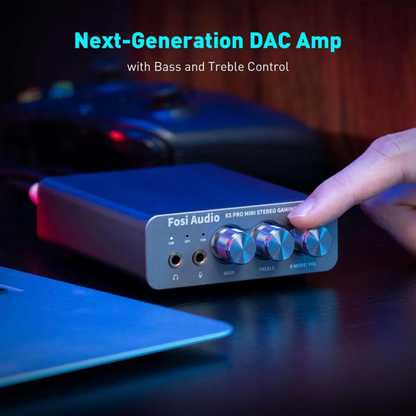 Fosi Audio DAC Amp with knobs on a dark surface, blurred gaming setup in the background
