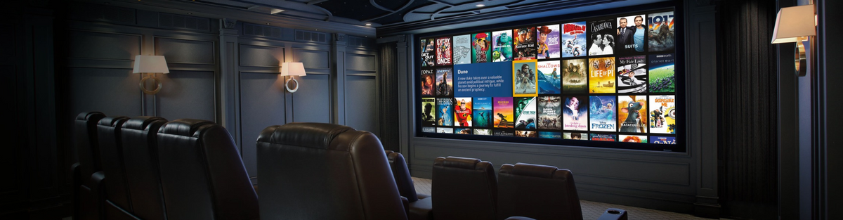 A home theater interior with dark leather recliners facing a large wall-mounted screen displaying a movie library interface.