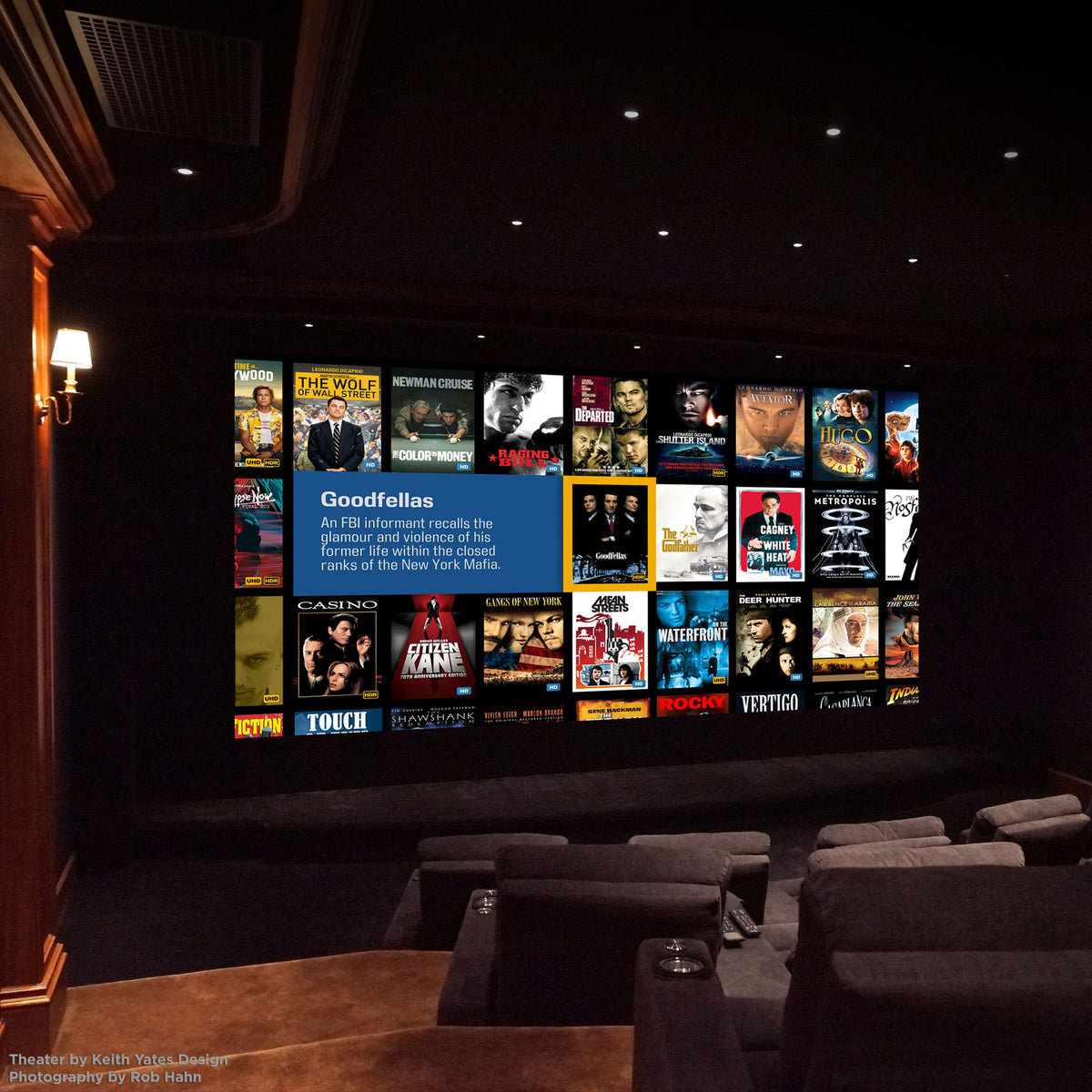 A home theater movie theater room with rows of dark gray theater seats facing a large projection screen displaying a movie lineup.