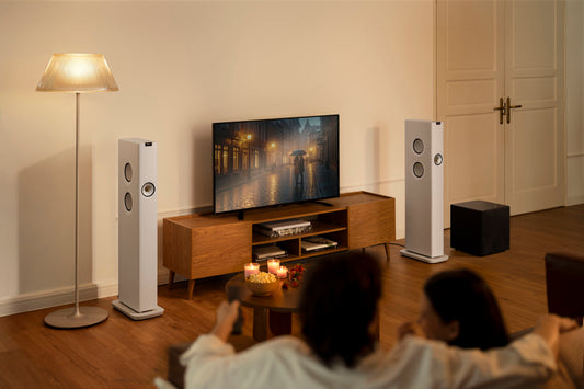 Living room setup with a TV, speakers, and people sitting on a couch.