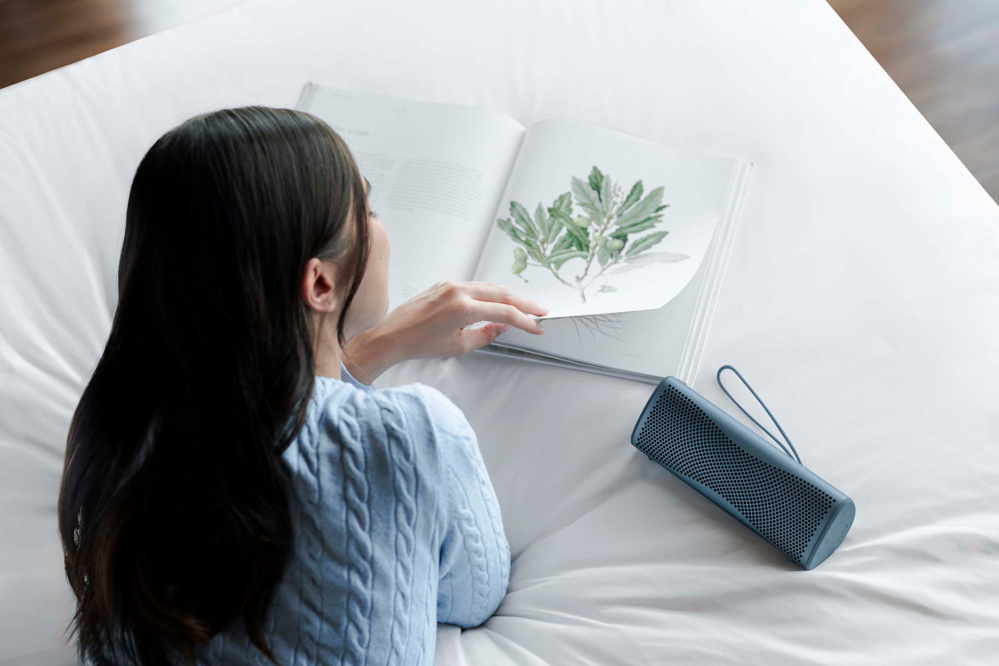 Person sitting on a bed with a plant illustration and a blue portable speaker.