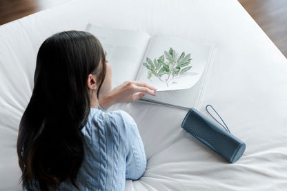 Person sitting on a bed with a plant illustration and a blue portable speaker.