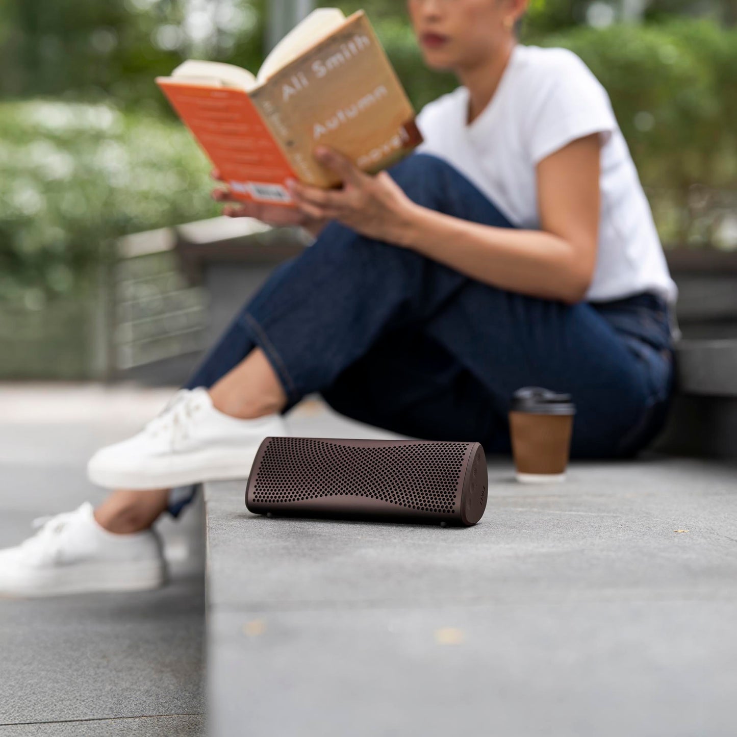 Person reading a book with a portable speaker on the ground nearby.