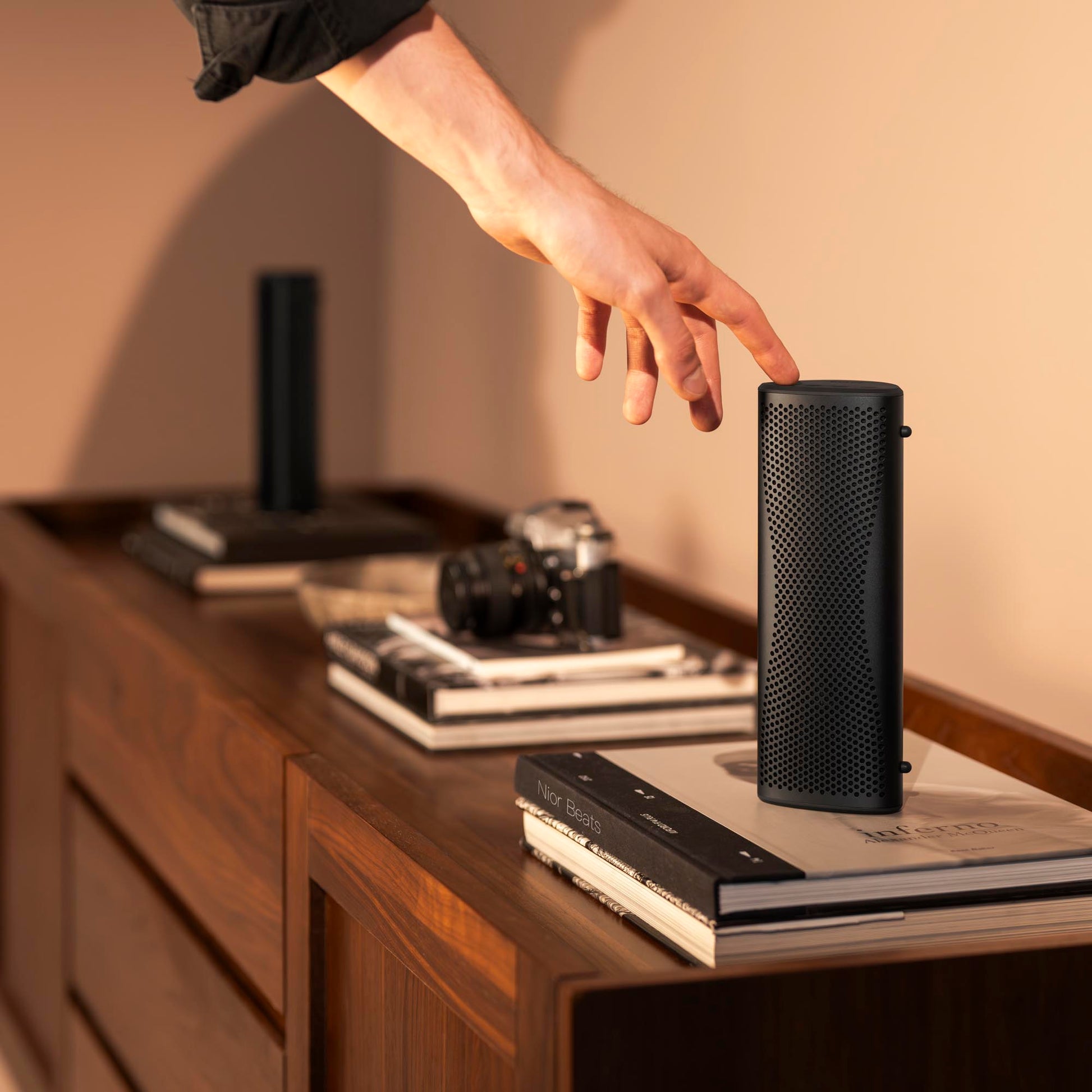 Person reaching out to touch a black Kef Muo Bluetooth Speaker on a wooden surface.