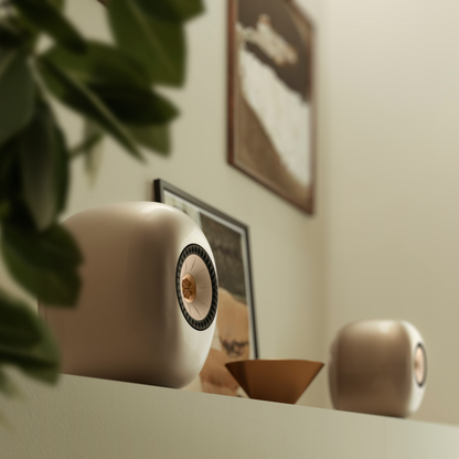 Two KEF LS LUXE Wireless Powered Speakers, styled on a shelf in a warm, modern room with a plant and framed art in the background.