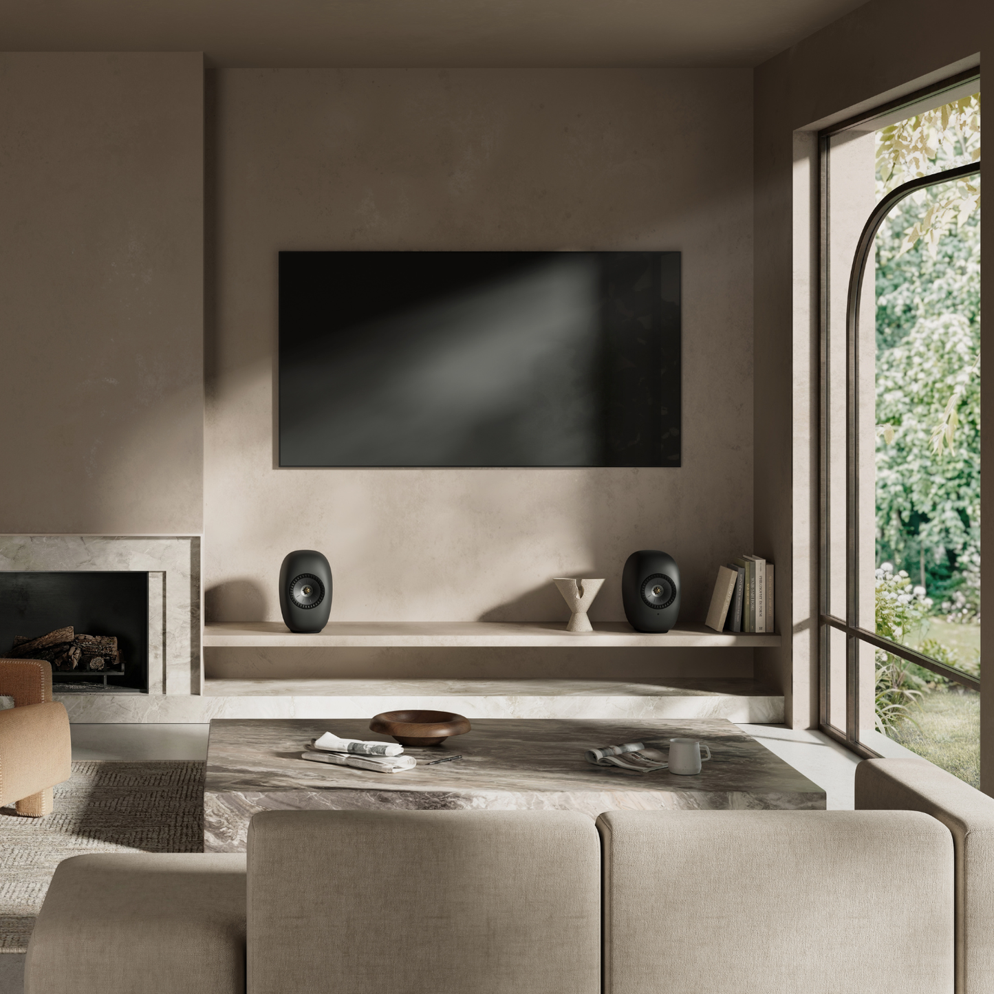 A modern living room interior with a large black rectangular wall-mounted screen centered above a low shelf. Two black oval speakers sit on the shelf, flanking a small sculptural vase.