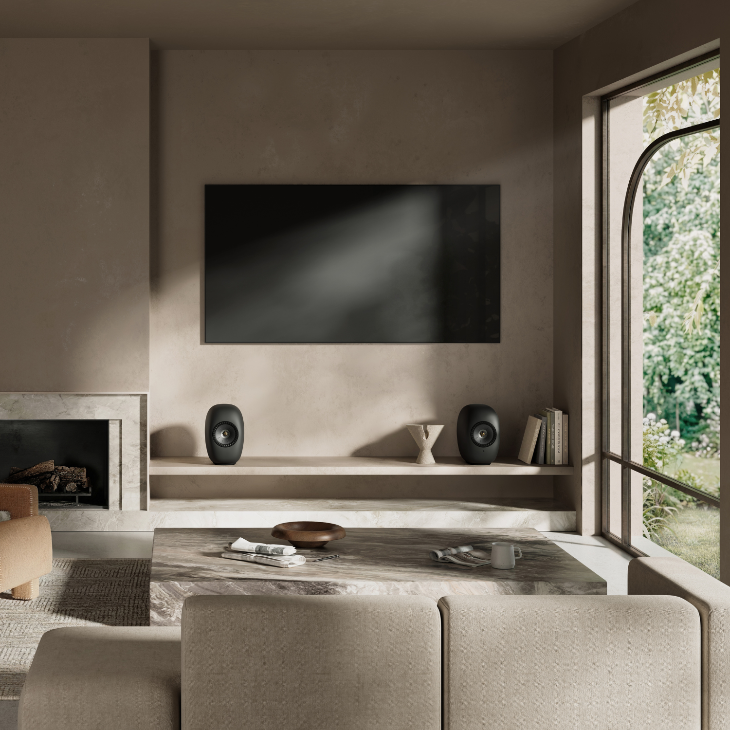 A modern living room interior with a large black rectangular wall-mounted screen centered above a low shelf. Two black oval speakers sit on the shelf, flanking a small sculptural vase.