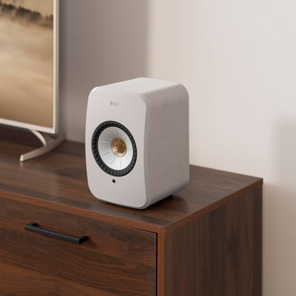White speaker on a wooden surface with a blurred television in the background