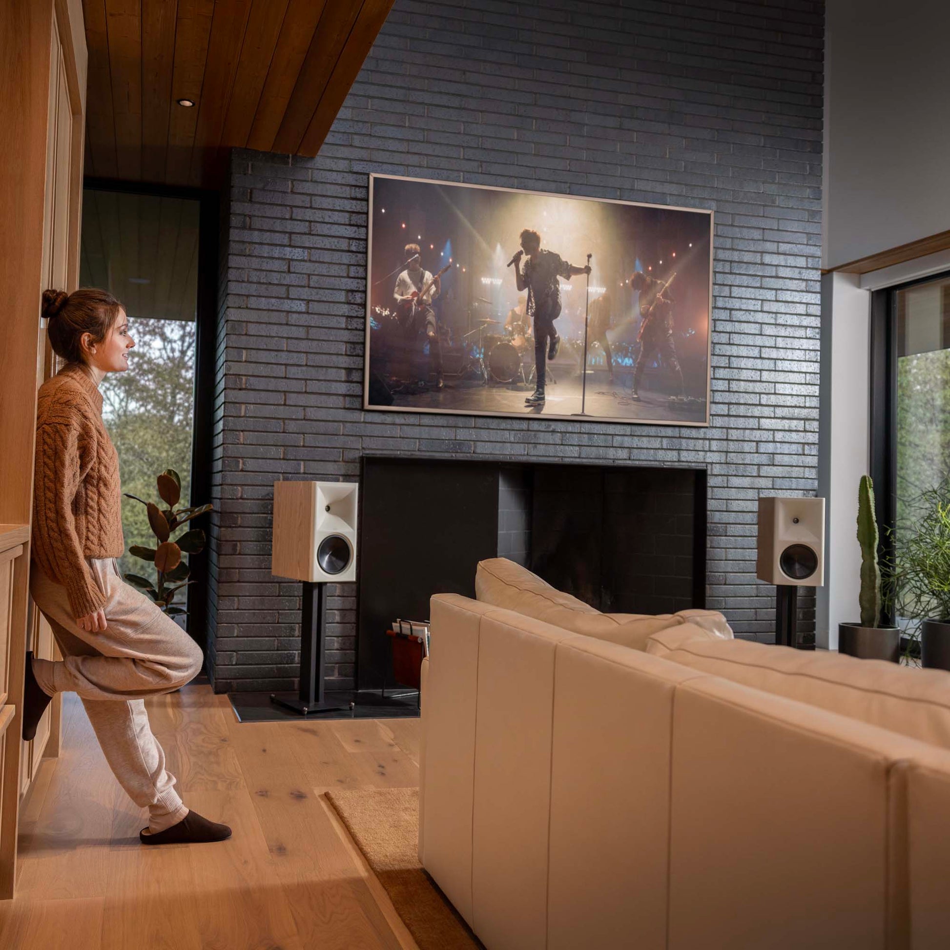 Woman leaning against wall in living room with white couch and Klipsch The Nines II Powered Speakers