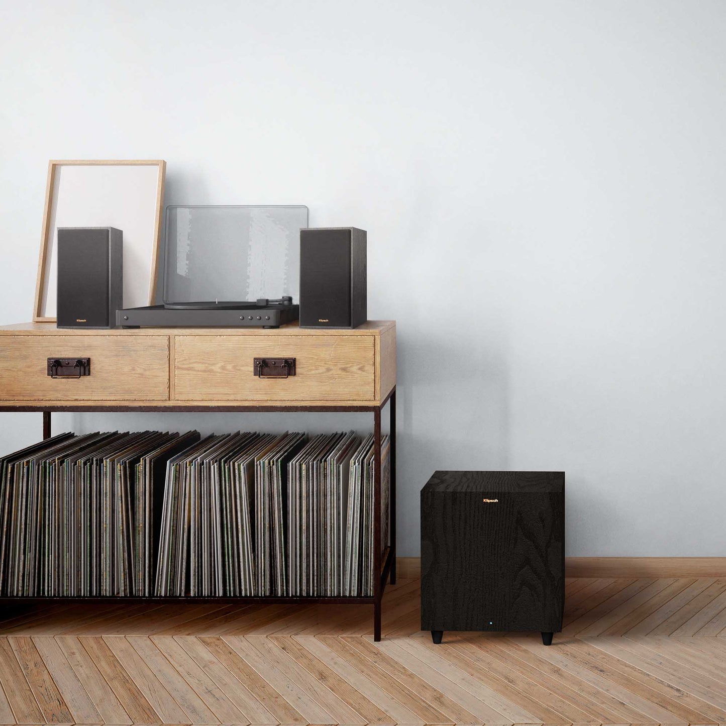 Music system with speakers and vinyl records on a wooden console against a white wall.