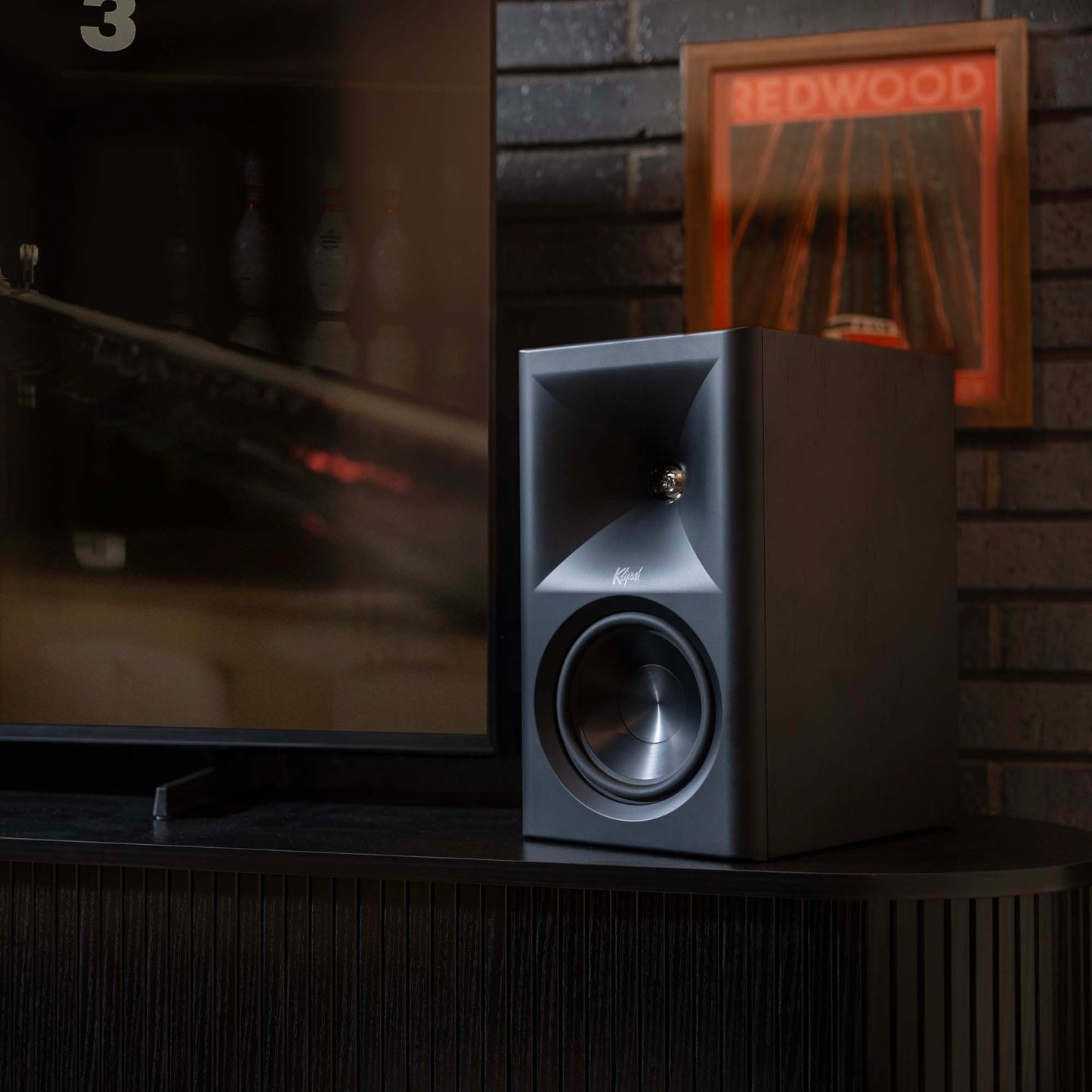 Speaker on a cabinet in a room with a television and framed picture in the background