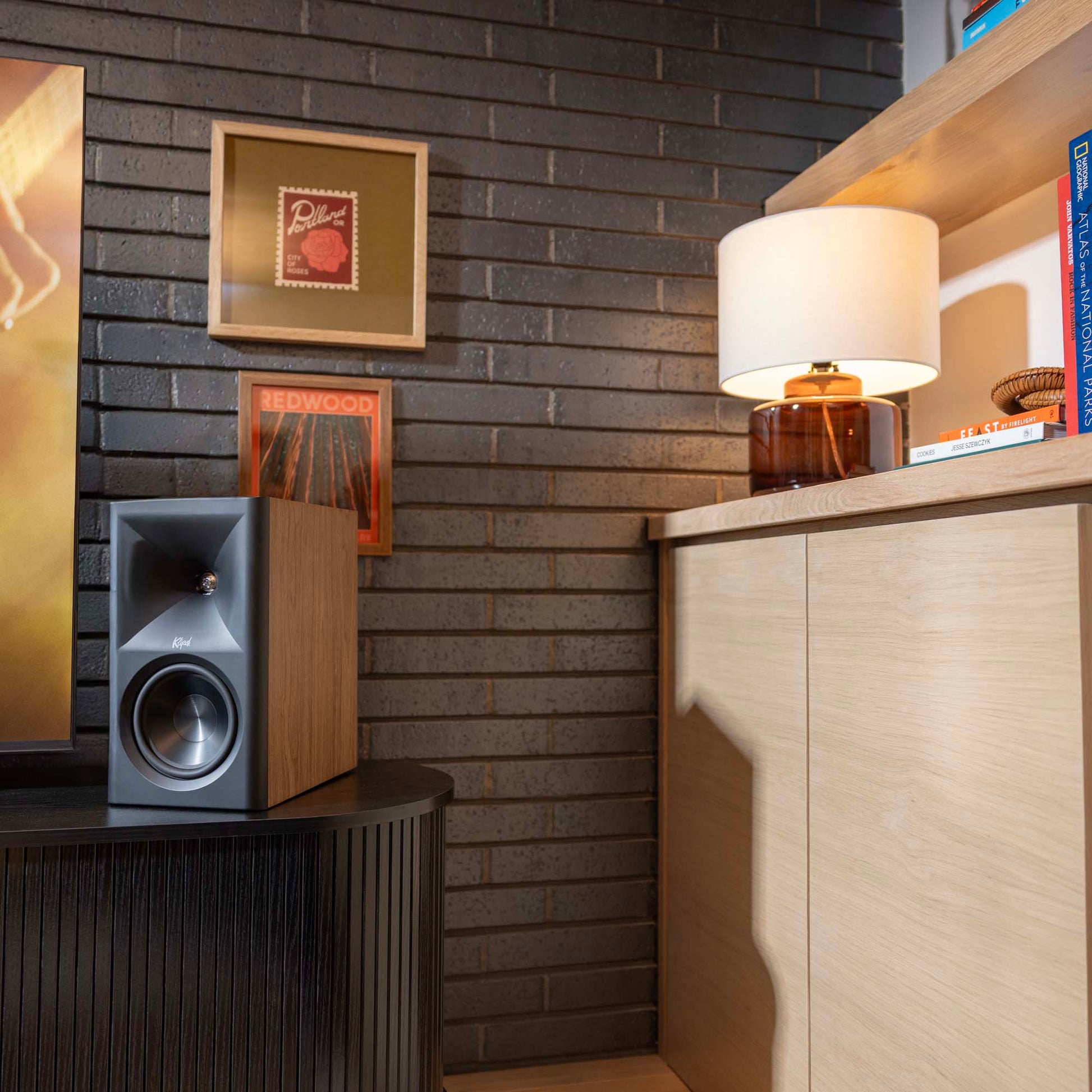 Modern interior with a speaker, lamp, and framed pictures on a brick wall.