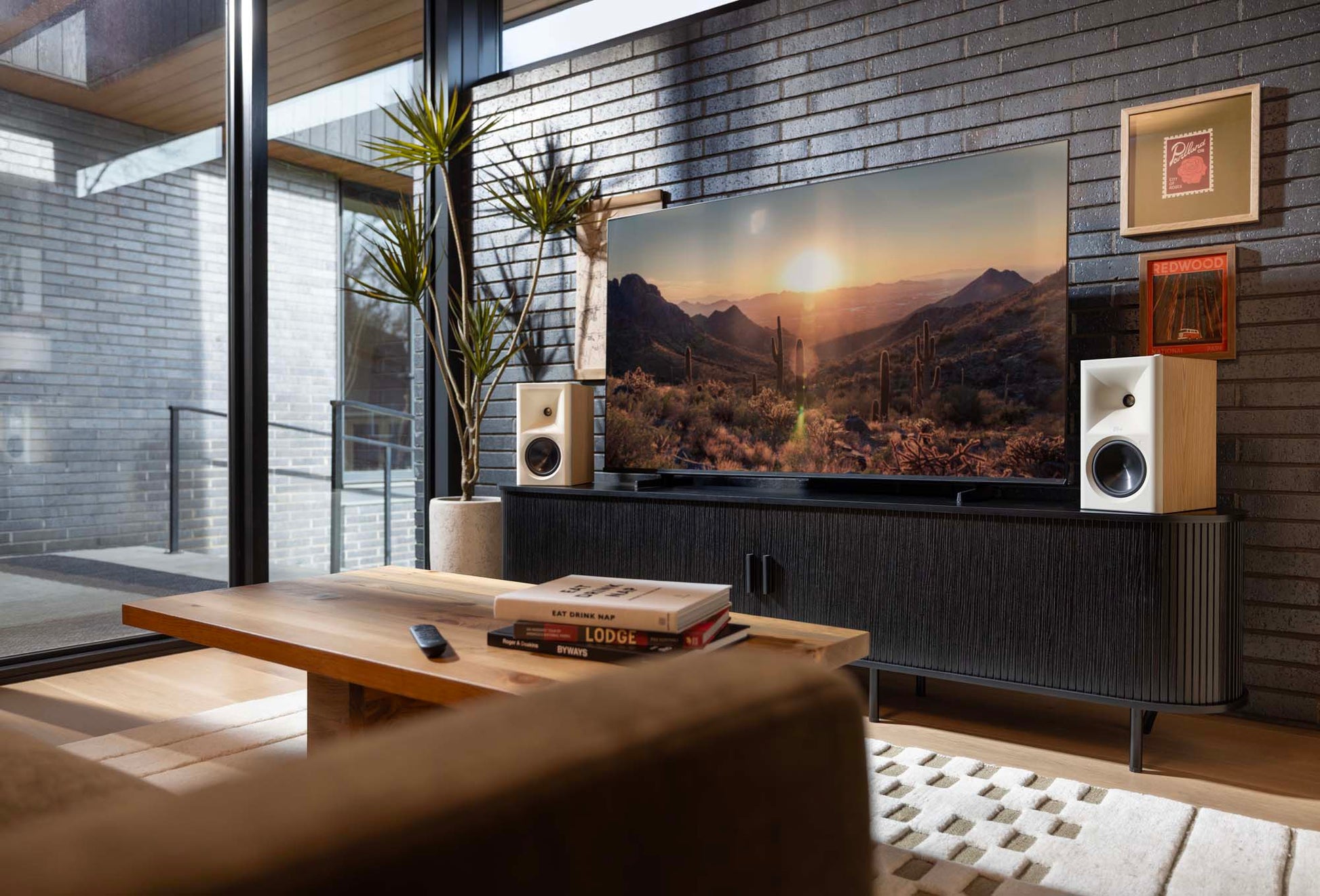 Modern living room with a large TV displaying a mountain scene, flanked by speakers and decor.