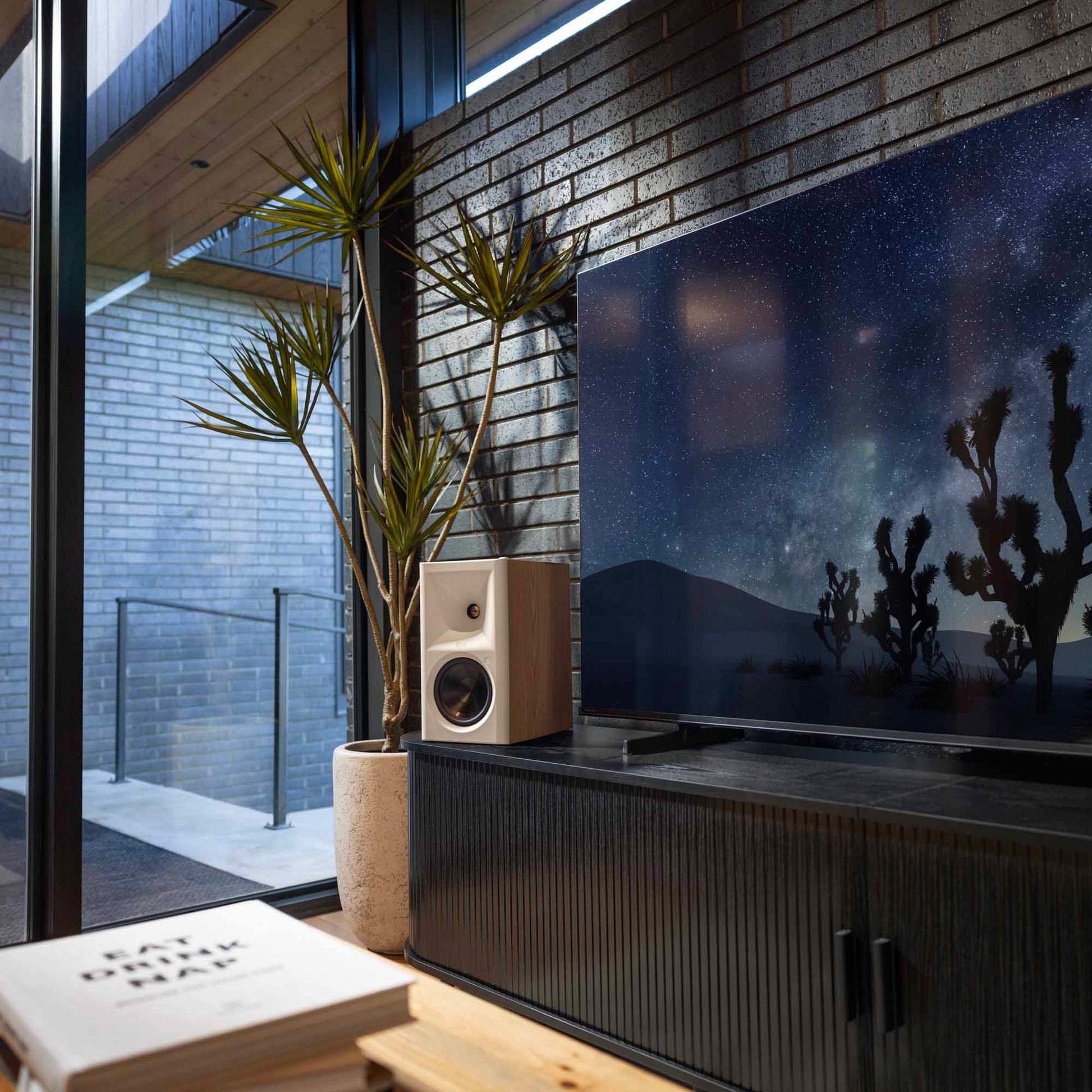 Modern living room with a large TV displaying a desert scene, speakers, and decorative plants.