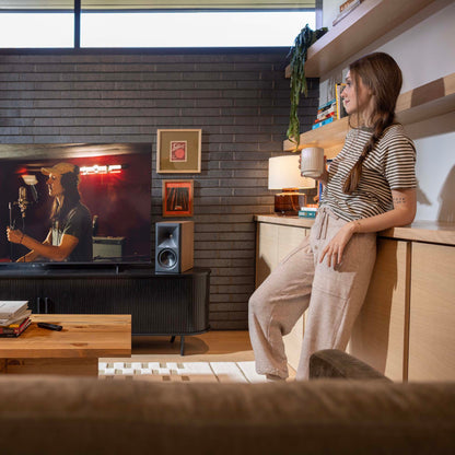 Woman standing next to a couch in a living room watching TV.