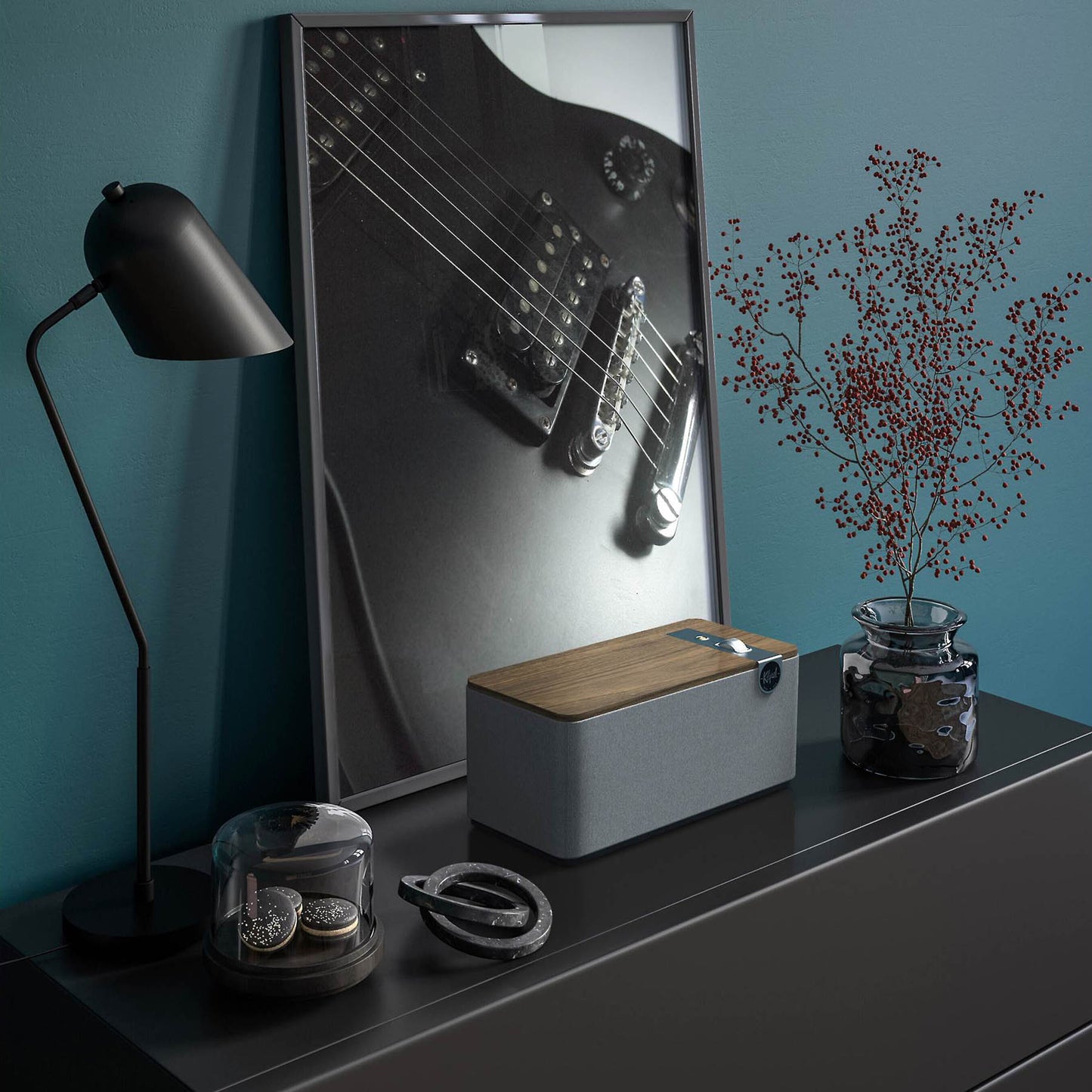 Decorative setup with a guitar poster, lamp, and Klipsch The One Plus in walnut on a shelf against a blue wall.