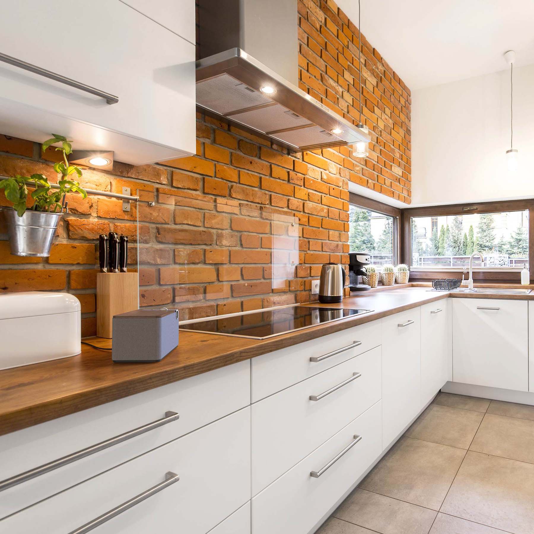 Modern kitchen with white cabinets, wooden countertops, and a brick wall. Klipsch The One Plus sitting on bench.