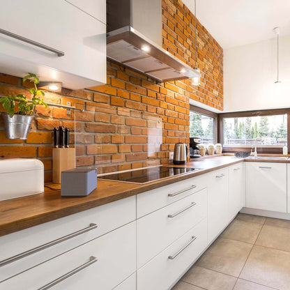Modern kitchen with white cabinets, wooden countertops, and a brick wall. Klipsch The One Plus sitting on bench.