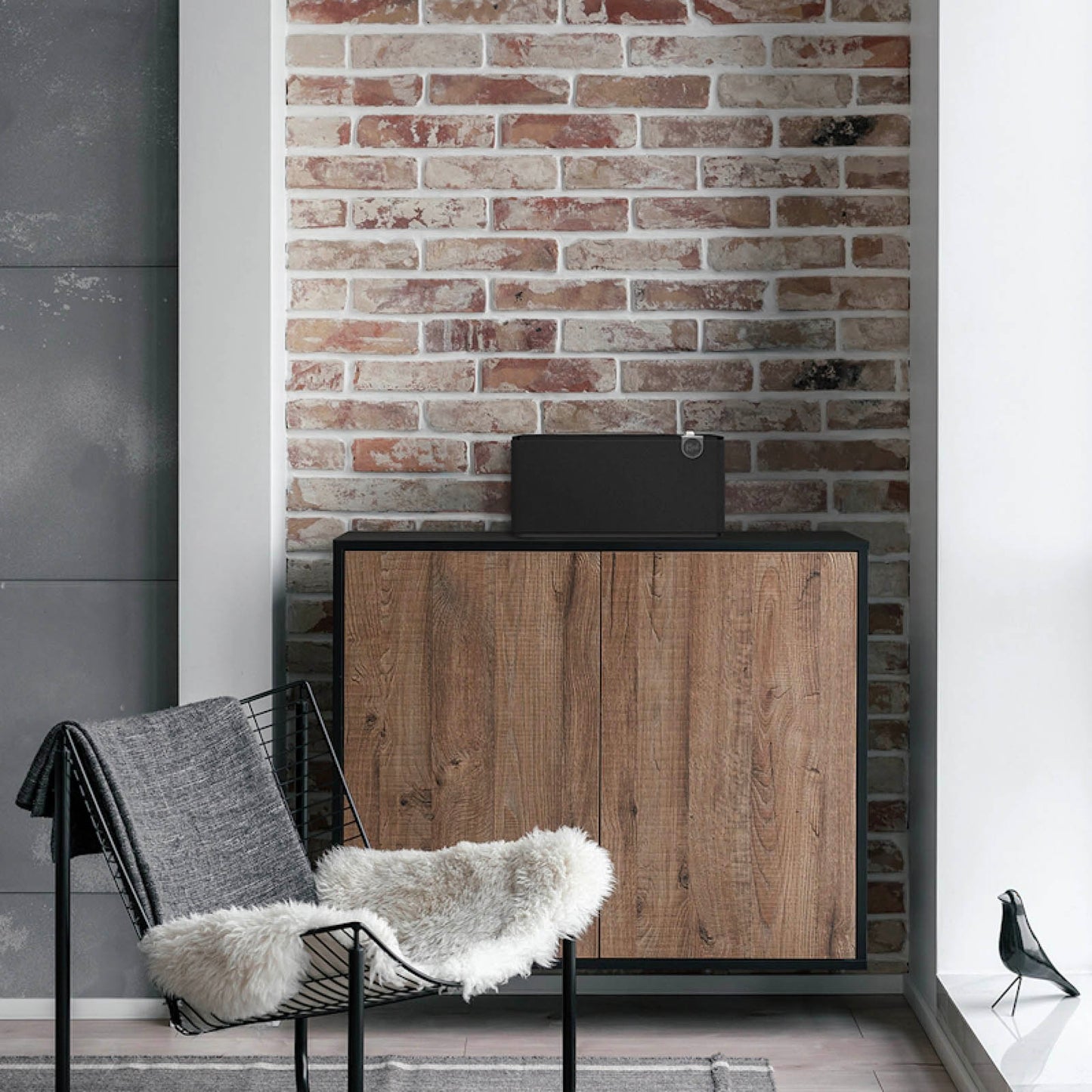 Black Klipsch The Three Plus Bluetooth Speaker sitting on cabinet against a brown brick wall
