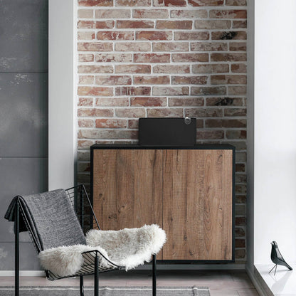Black Klipsch The Three Plus Bluetooth Speaker sitting on cabinet against a brown brick wall