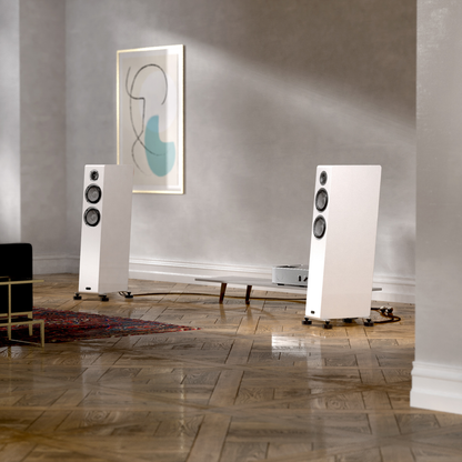 White floor-standing speakers in a room with a painting on the wall.