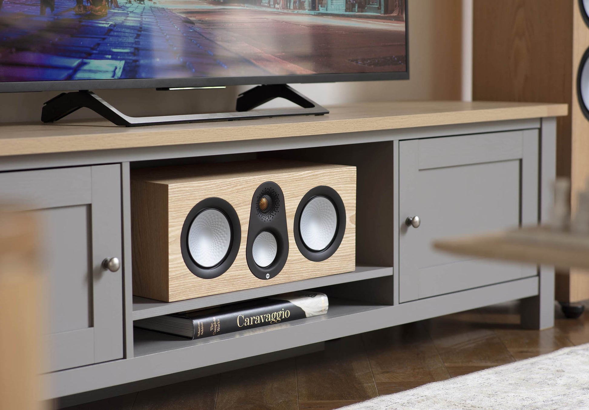 Wooden centre speaker on a TV stand with a television in the background
