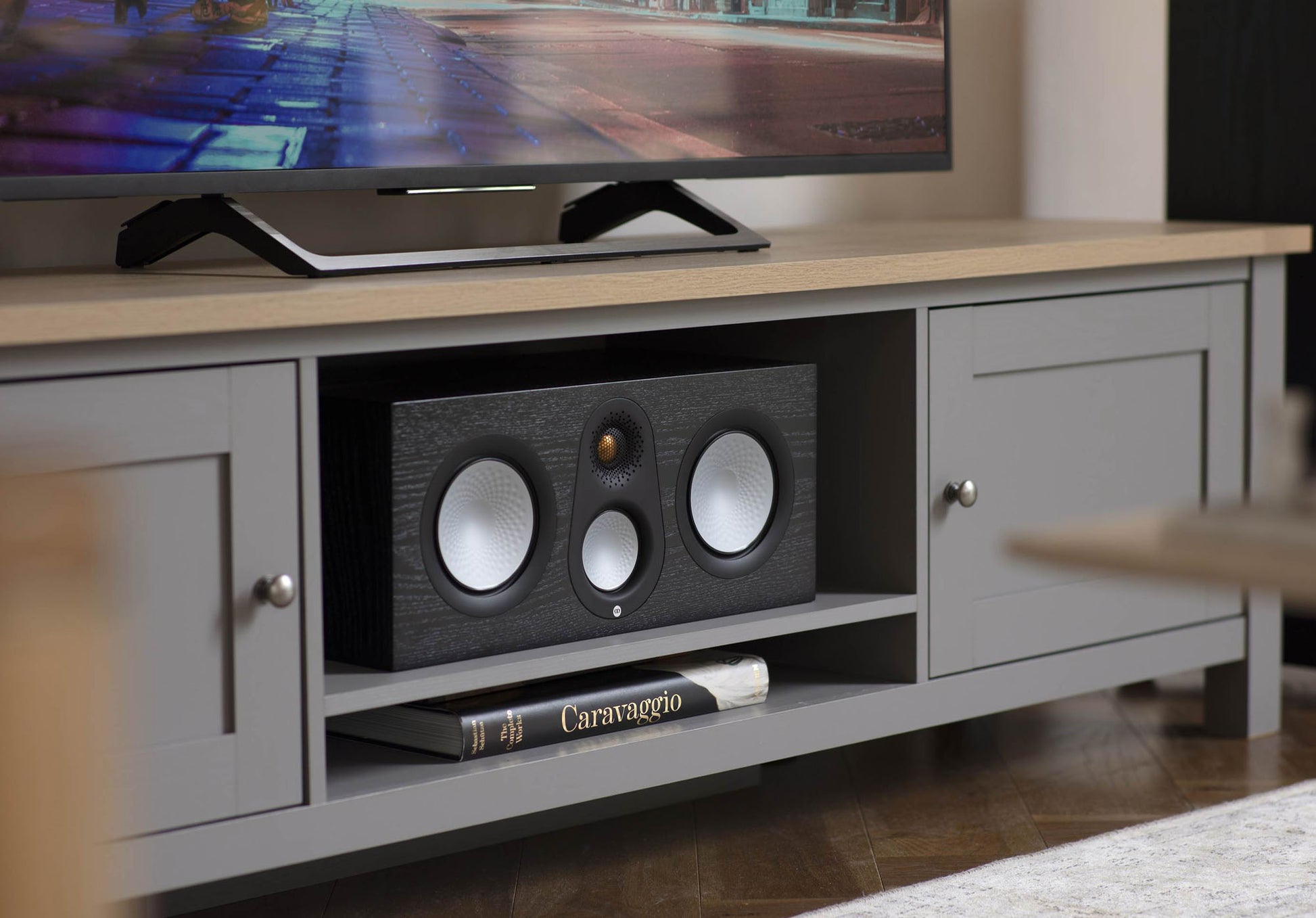 TV on a wooden stand with a speaker and book in a living room setting
