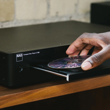 Hand placing a CD into a NAD compact disc player on a wooden surface.