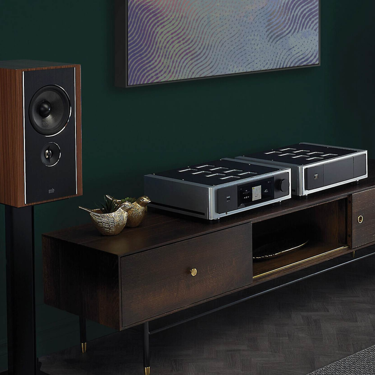 Modern home entertainment system with speakers and NAD Masters M66 on a wooden console against a dark wall.