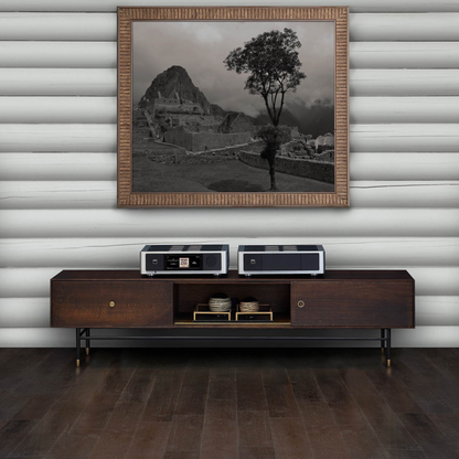 Wooden entertainment console with audio equipment against a wall with a framed black and white landscape.