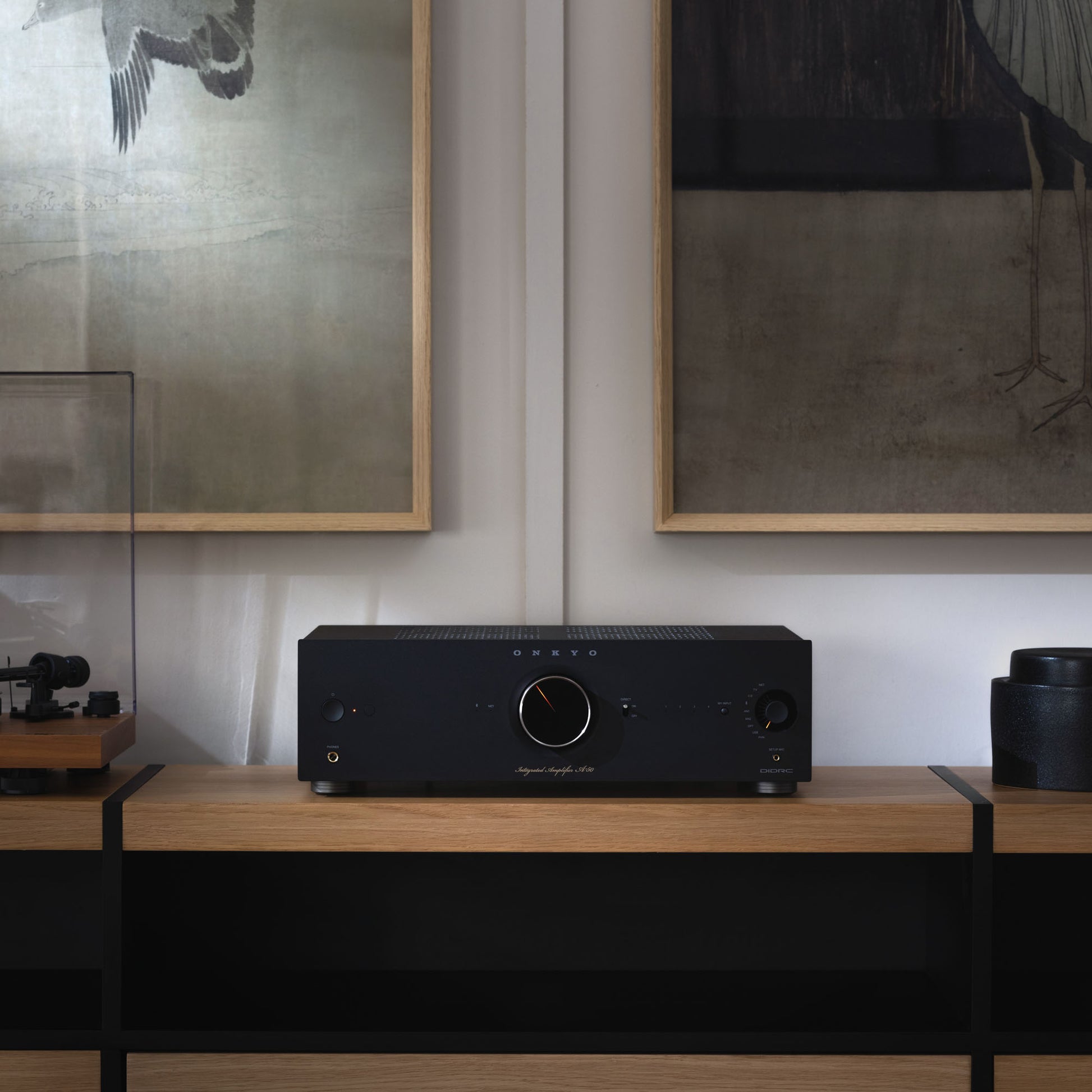 Black audio amplifier on a wooden surface with framed artwork in the background