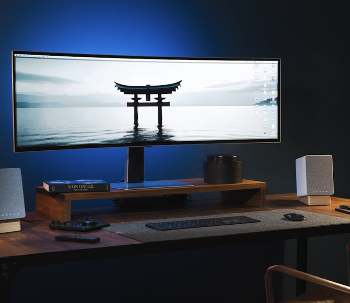Modern desk setup with a large monitor displaying a scenic image, keyboard, and speakers in a dark room.