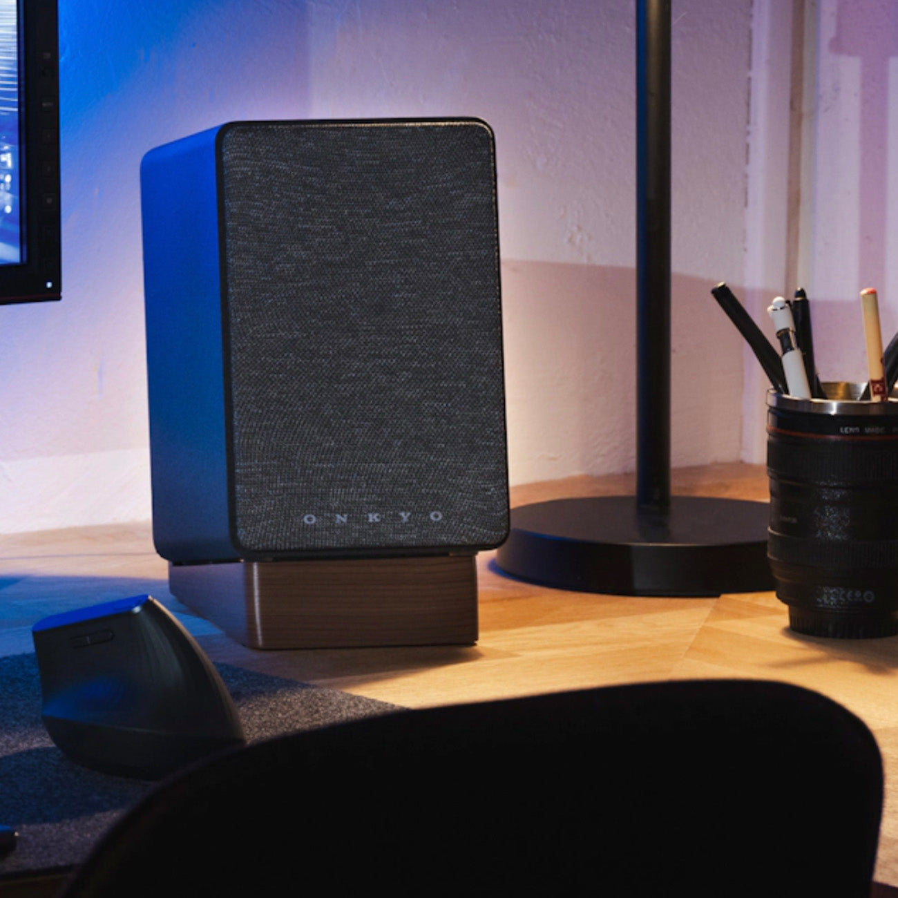 Black speaker on a wooden desk with office supplies in the background